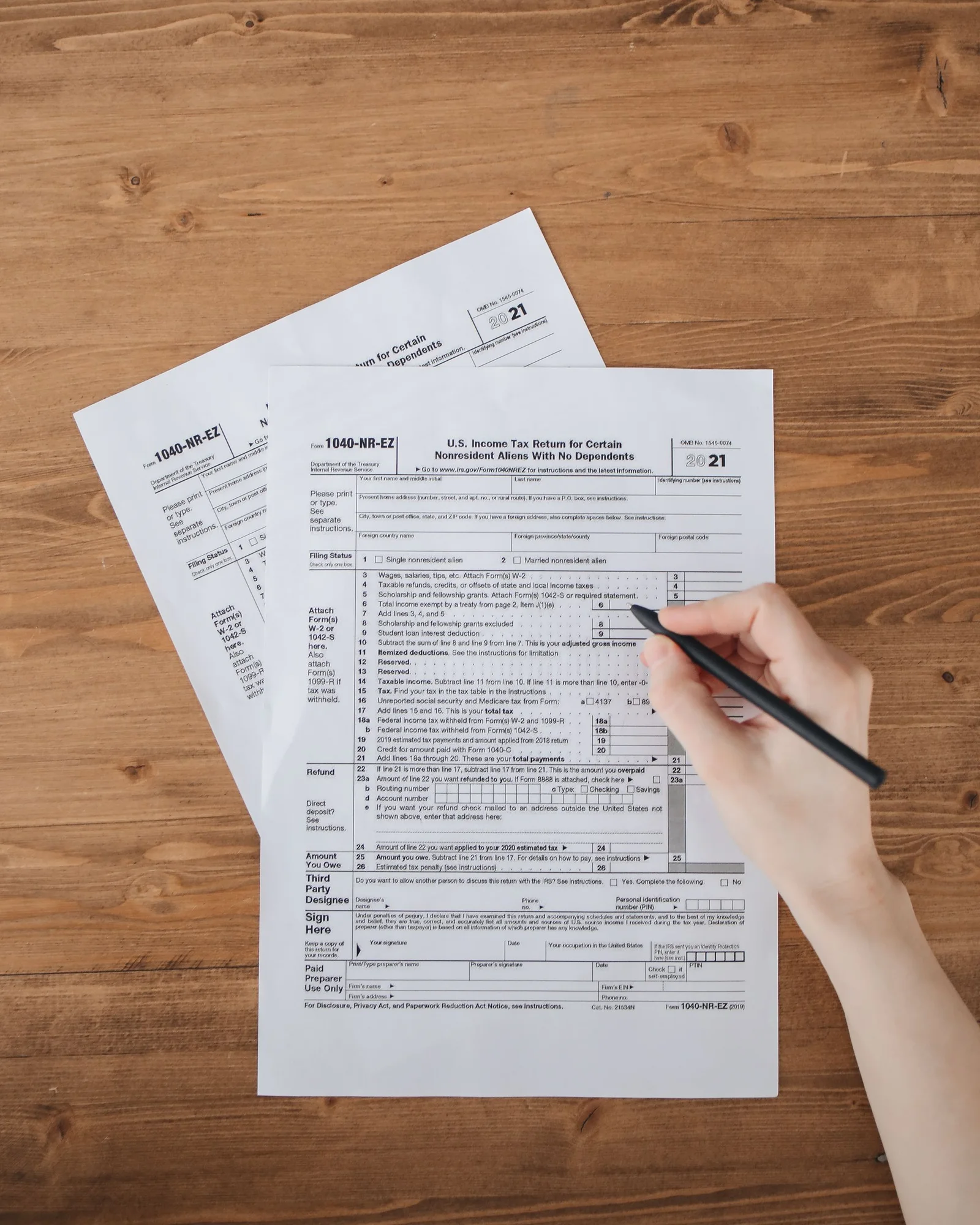 Une main remplit au stylo le formulaire de déclaration, posé sur un bureau en bois